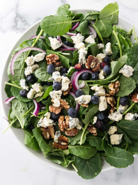 A large salad bowl filled with greens, blueberries, red onion slices and roasted walnuts.