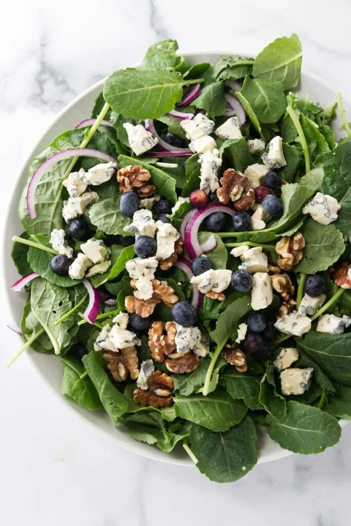 A large salad bowl filled with greens, blueberries, red onion slices and roasted walnuts.