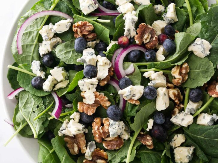 A large salad bowl filled with greens, blueberries, red onion slices and roasted walnuts.