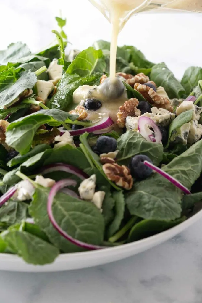 Pouring a lemon vinaigrette on a baby kale salad.