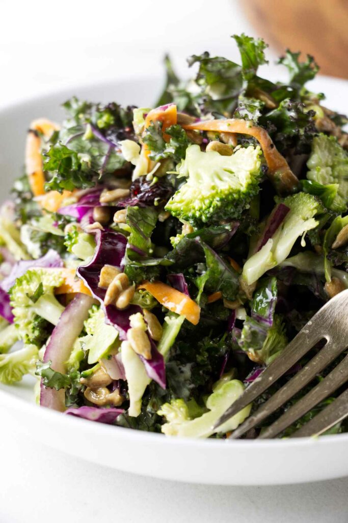 A kale and broccoli salad in a white bowl.