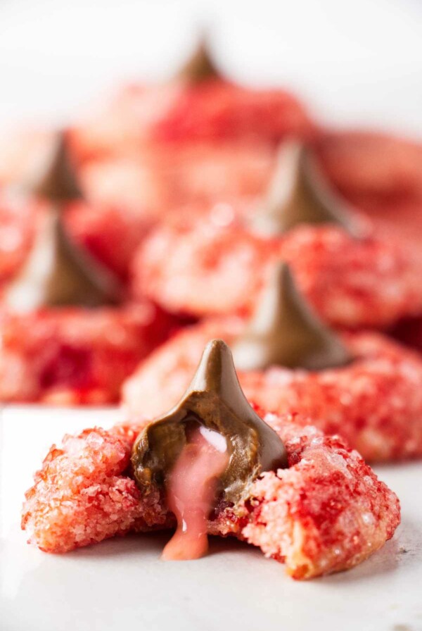 A partially eaten cookie with a cherry filled Hershey's kiss. The cherry center is oozing out of the chocolate candy.