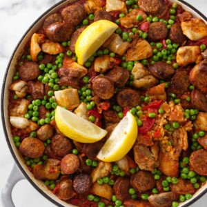 A large skillet filled with chicken and chorizo paella with lemon wedges on top.