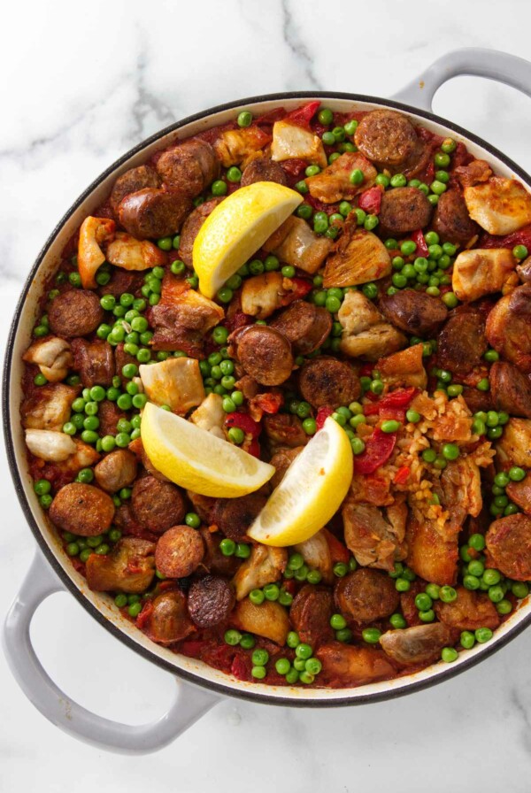 A large skillet filled with chicken and chorizo paella with lemon wedges on top.