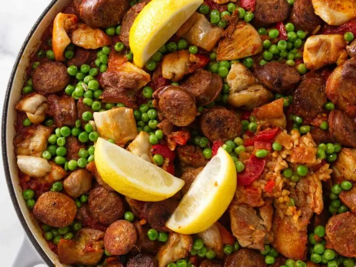 A large skillet filled with chicken and chorizo paella with lemon wedges on top.