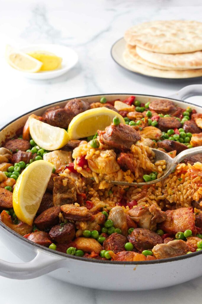 A spoon scooping chicken and chorizo paella out of a pan.