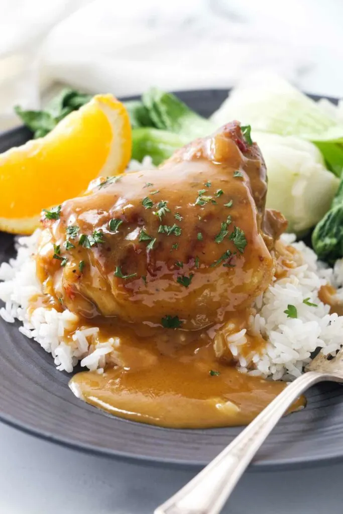 Star anise chicken with orange sauce on a plate with rice and veggies.