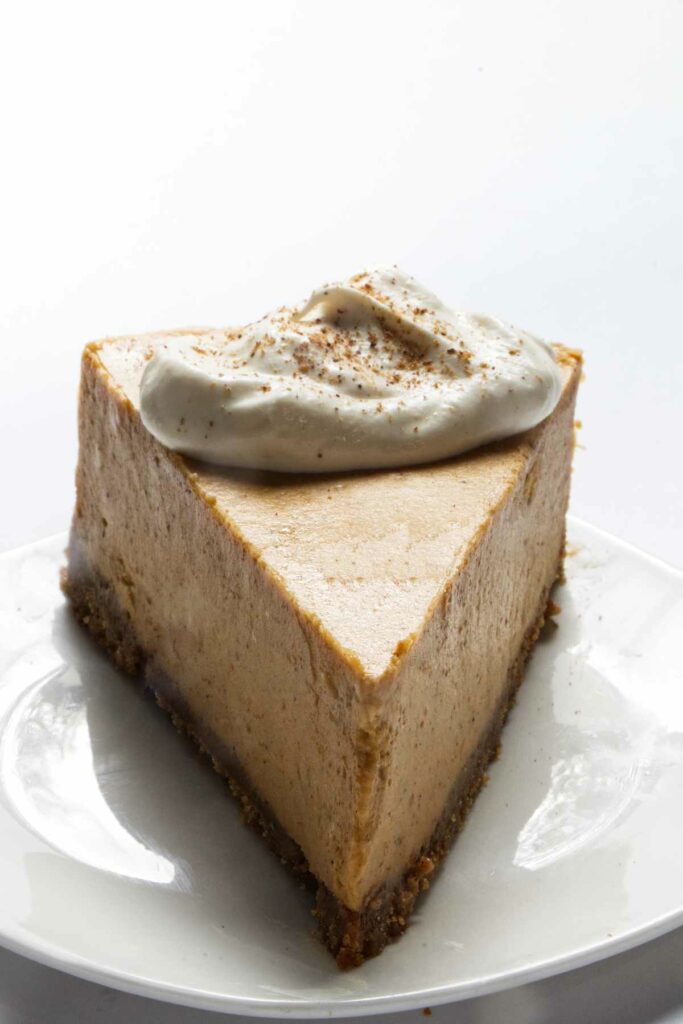 A slice of pumpkin cheesecake with whipped cream on top.