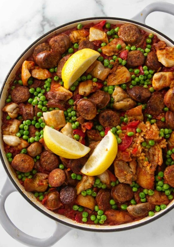 A large skillet filled with chicken and chorizo paella with lemon wedges on top.