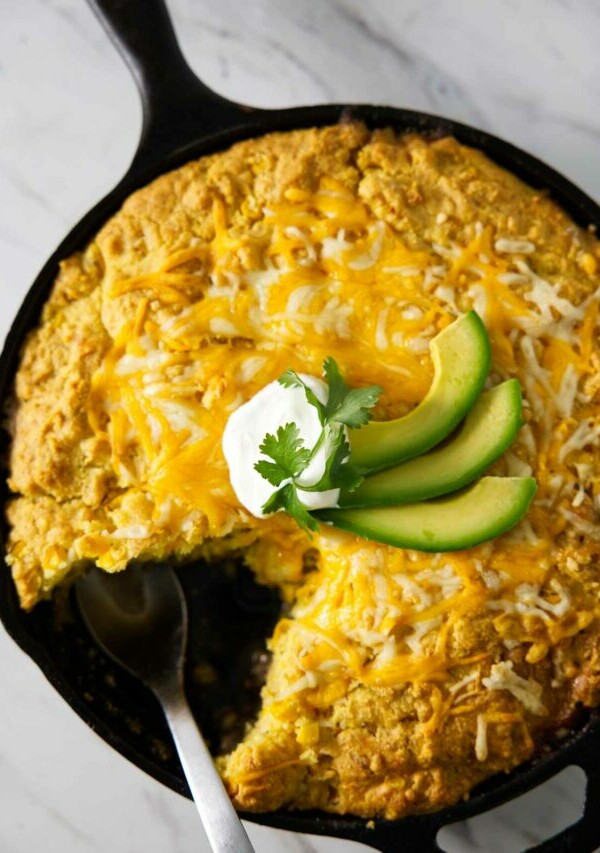 A green chili tamale pie in a skillet with sour cream and avocado slices on top.