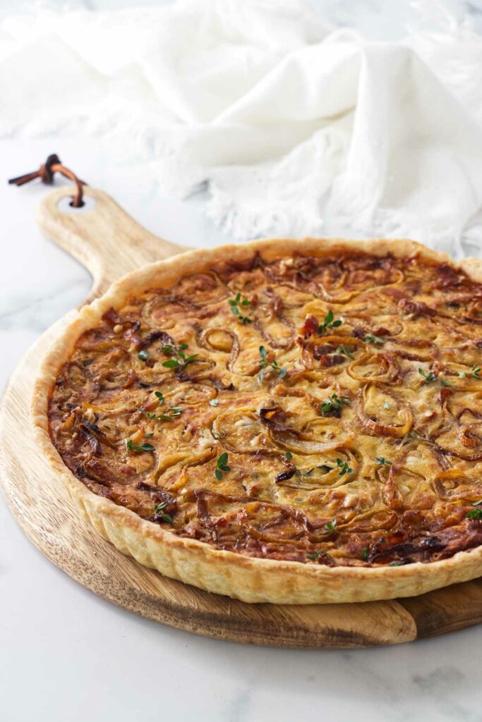 A baked onion tart on a wooden cutting board.
