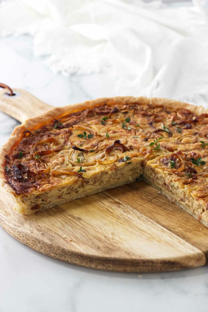 A sliced French onion tart on a wooden cutting board.