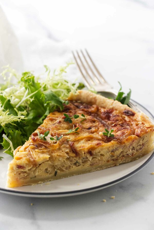 A serving of French onion tart on a plate with a fork. Green salad in the background.