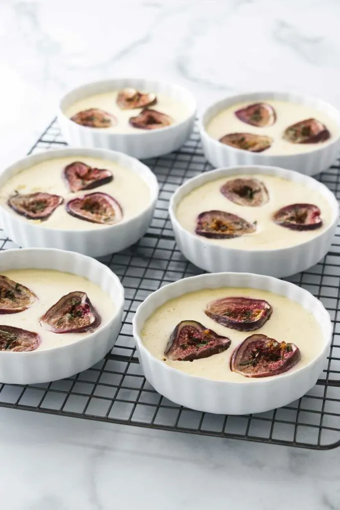 Six small dishes filled with custard and topped with roasted figs, sitting on a wire cooling rack.