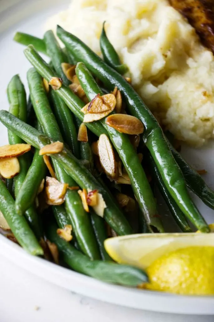 Green beans with toasted almonds and brown butter on a dinner plate.
