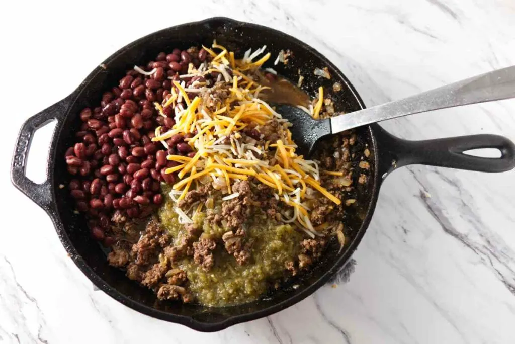 Adding black beans, salsa, and cheese to the ground beef mixture.