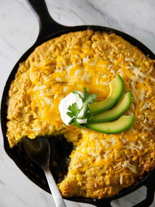 A green chili tamale pie in a skillet with sour cream and avocado slices on top.