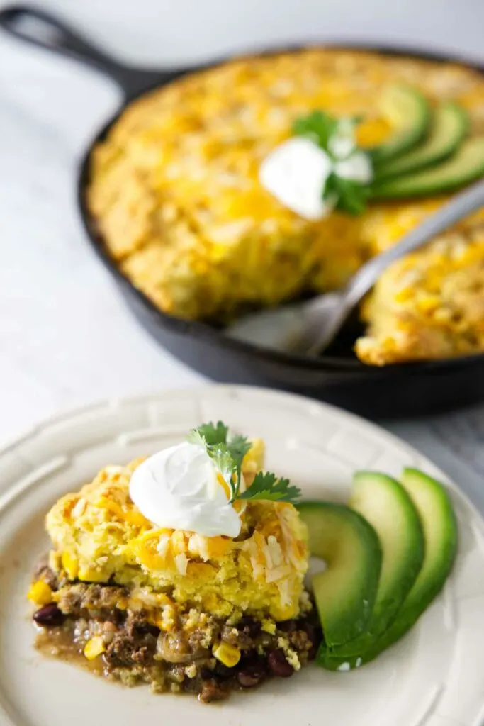 A serving of tamale pie on a plate with a skillet in the background.