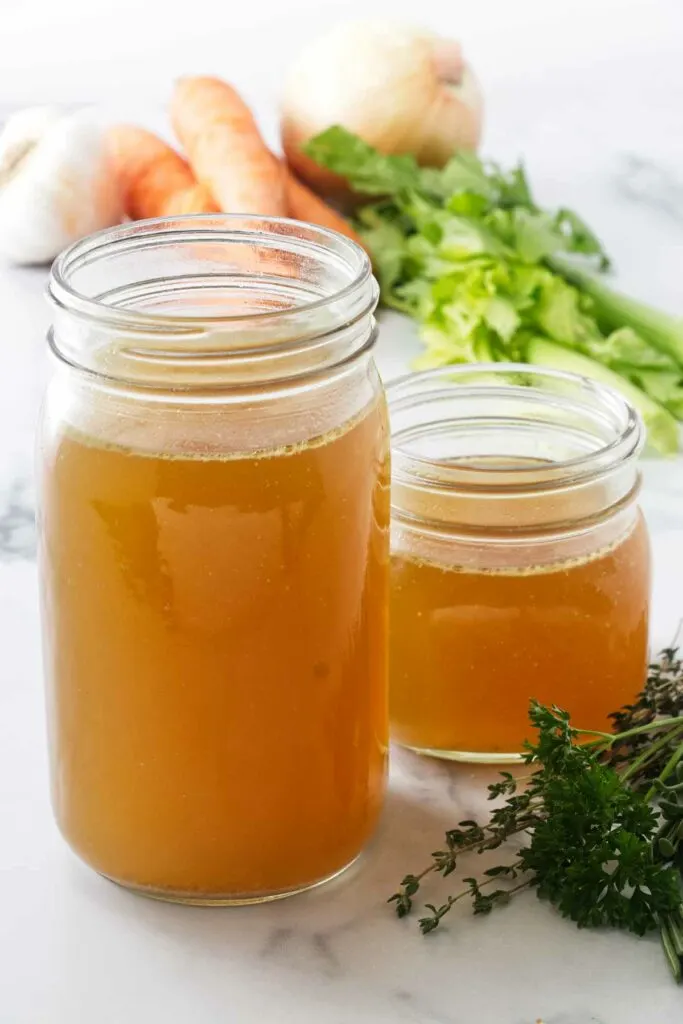 One quart, plus one pint of turkey broth. Fresh herbs in the foreground and vegetables in the background.