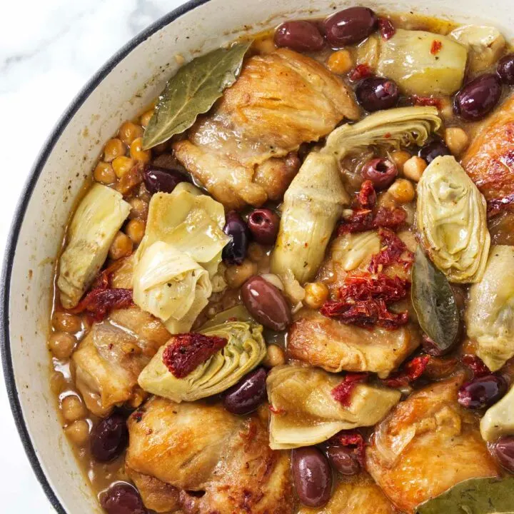 Pot with chicken, artichokes, olives, sun-dried tomatoes and garbanzo beans in a sauce.