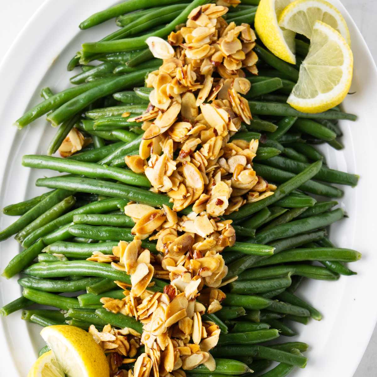 Green beans with almonds and brown butter on a serving plate with lemon slices.