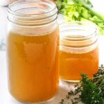 One quart, plus one pint of turkey broth. Fresh herbs in the foreground and vegetables in the background.