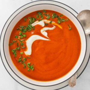 A bowl filled with roasted red pepper soup and garnished with cream and chives.