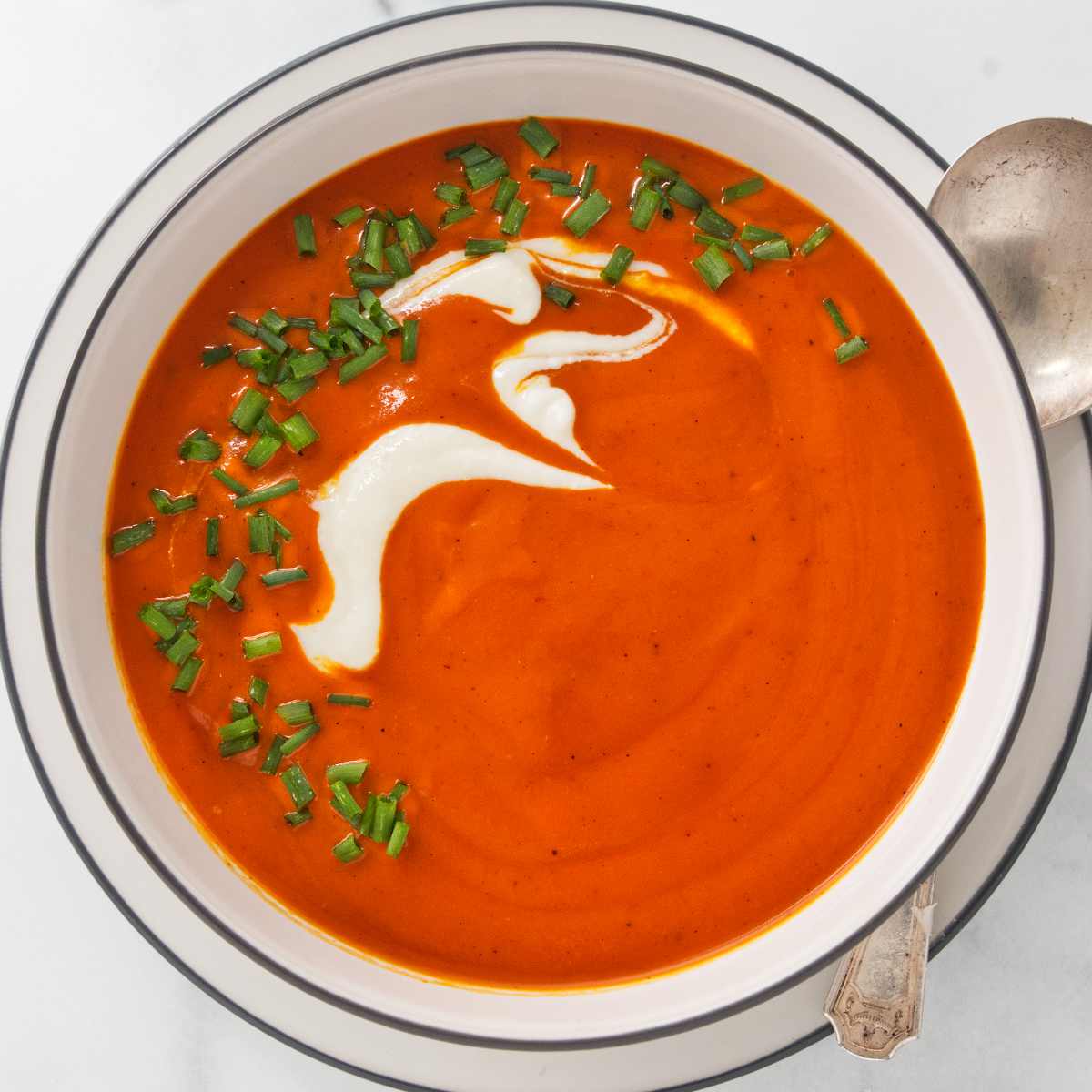 A bowl filled with roasted red pepper soup and garnished with cream and chives.