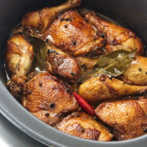 Chicken thighs and chicken legs in a slow cooker with a red chili, peppercorns and bay leaves.