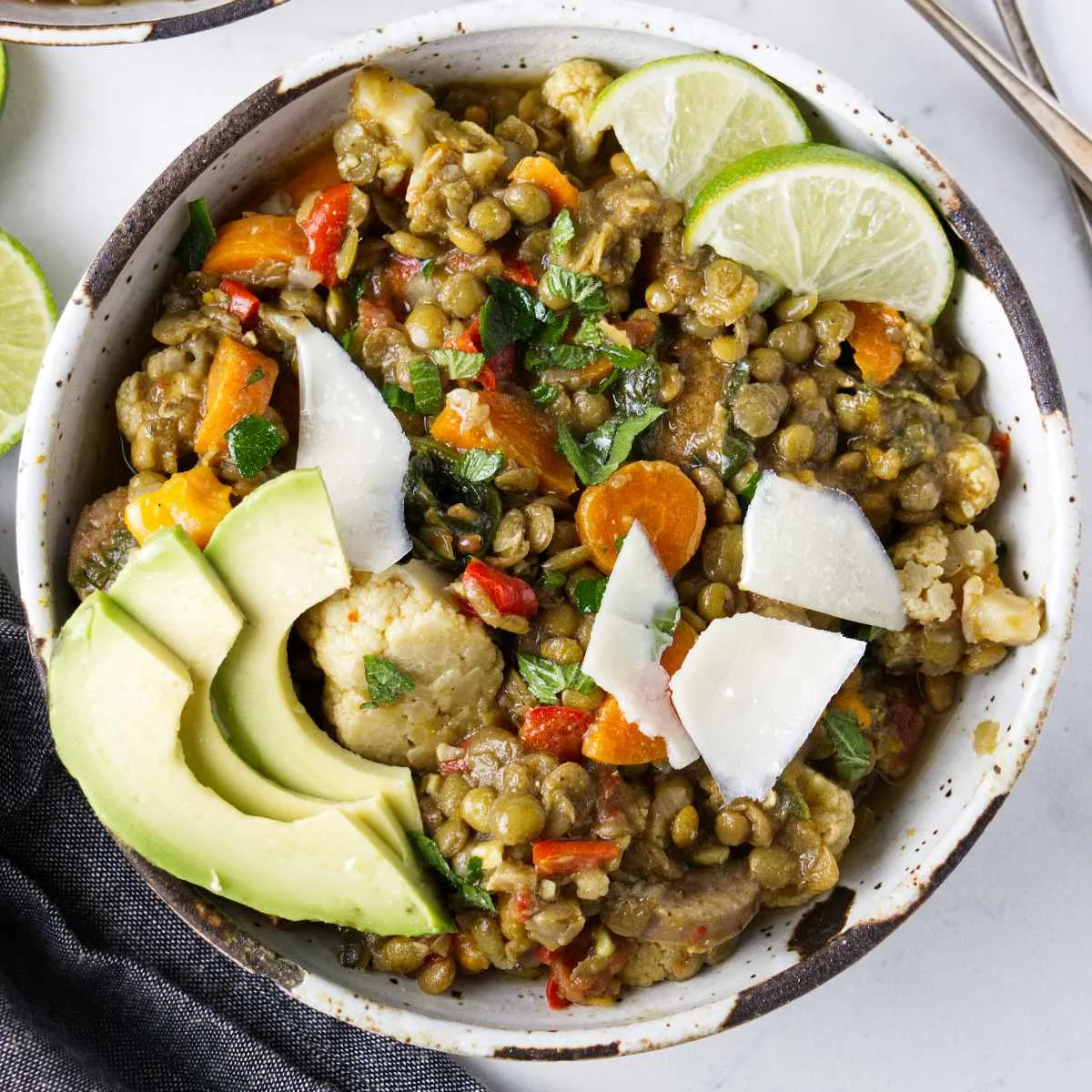 A bowl of lentil stew topped with slices of lime and avocado.
