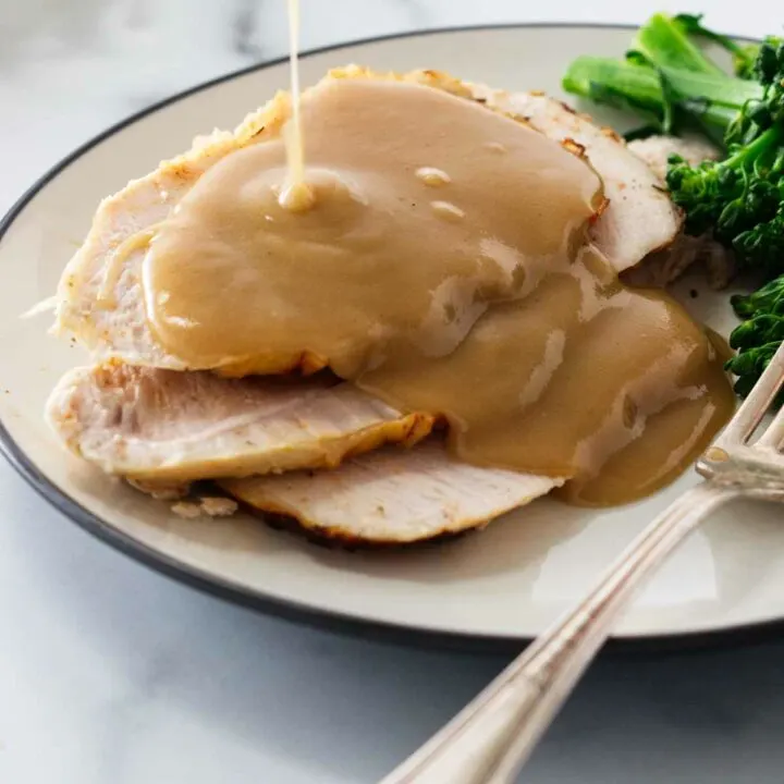 Pouring turkey gravy over slices of turkey on a plate.