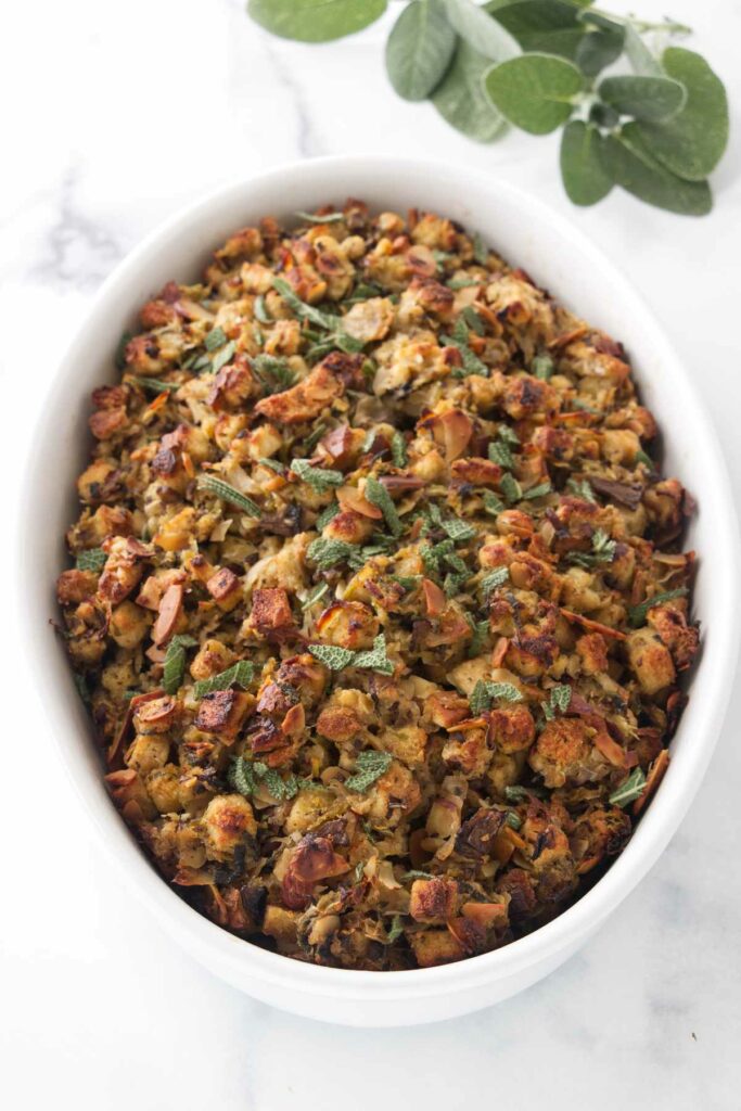 An overhead view of a dish of baked stuffing garnished with chopped sage. Fresh sage leaves in the background.