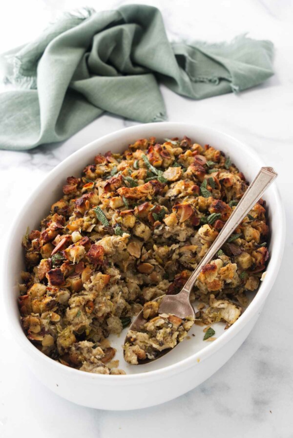 A dish of stuffing with a serving spoon, a kitchen towel in the background.