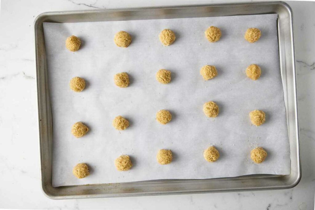 Twenty round balls of cookie dough on a baking sheet.