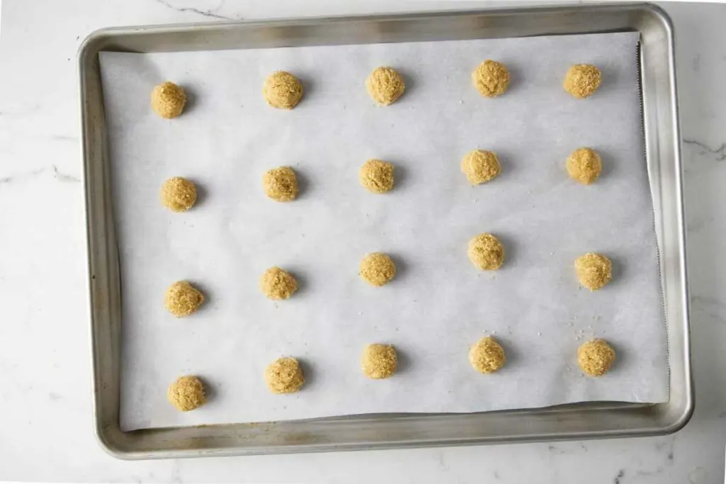Twenty round balls of cookie dough on a baking sheet.