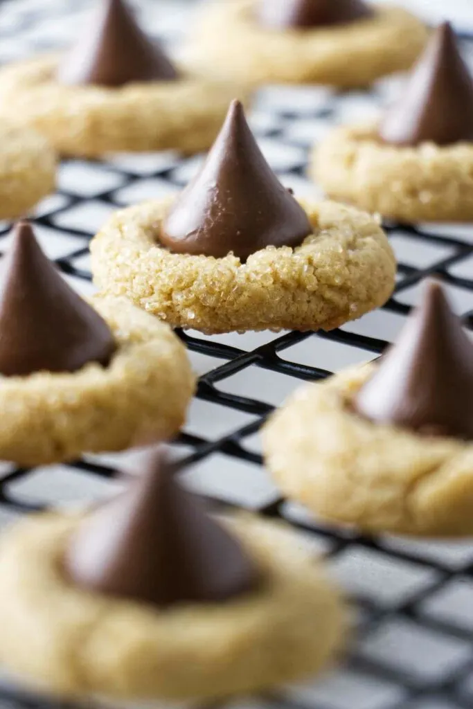 Peanut butter cookies with a chocolate kiss candy in the center. The cookies are on a cooling rack.