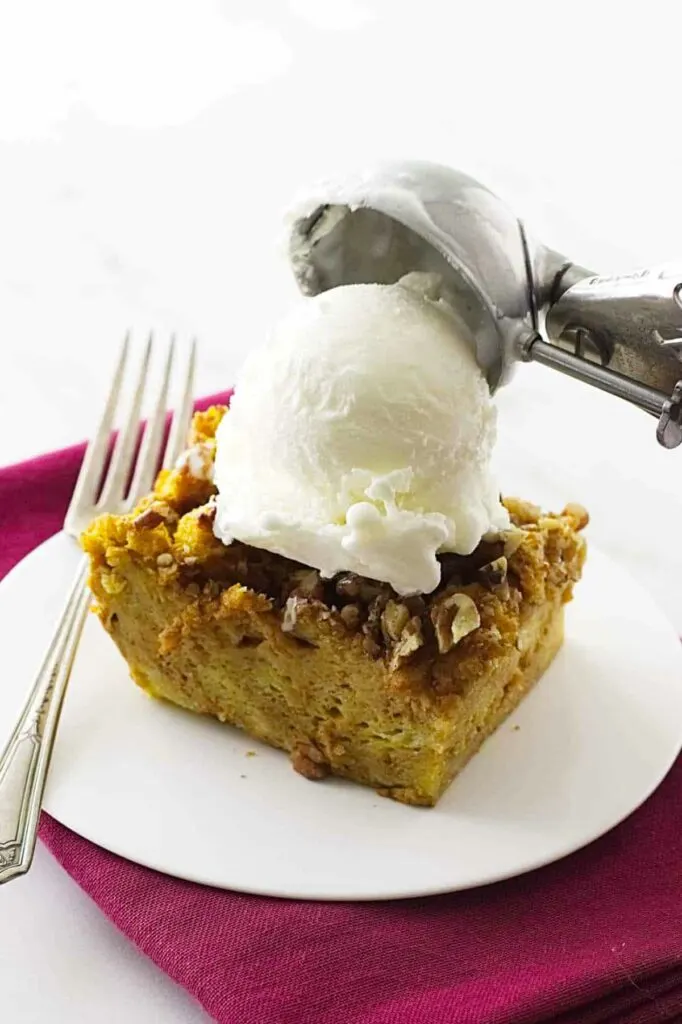 pumpkin bread pudding on a saucer with vanilla ice cream on top.