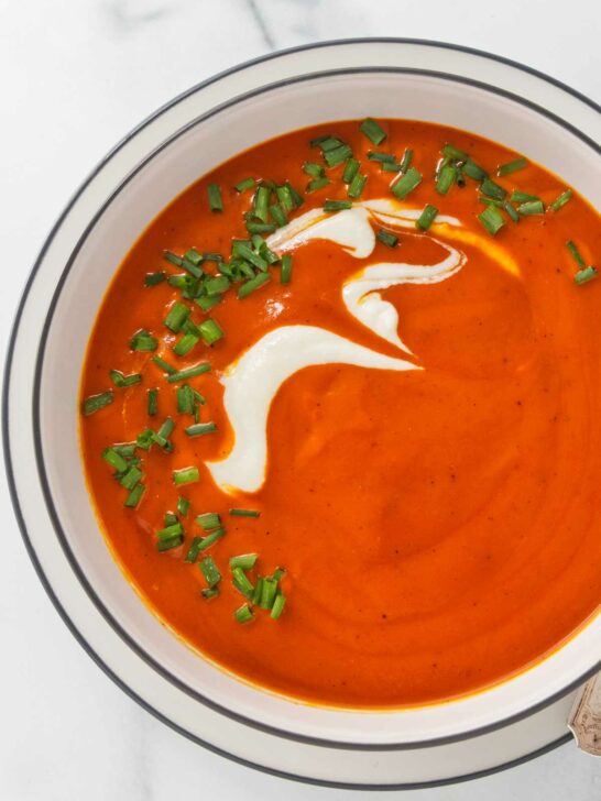 Roasted red pepper soup in a white bowl and garnished with cream and chives.