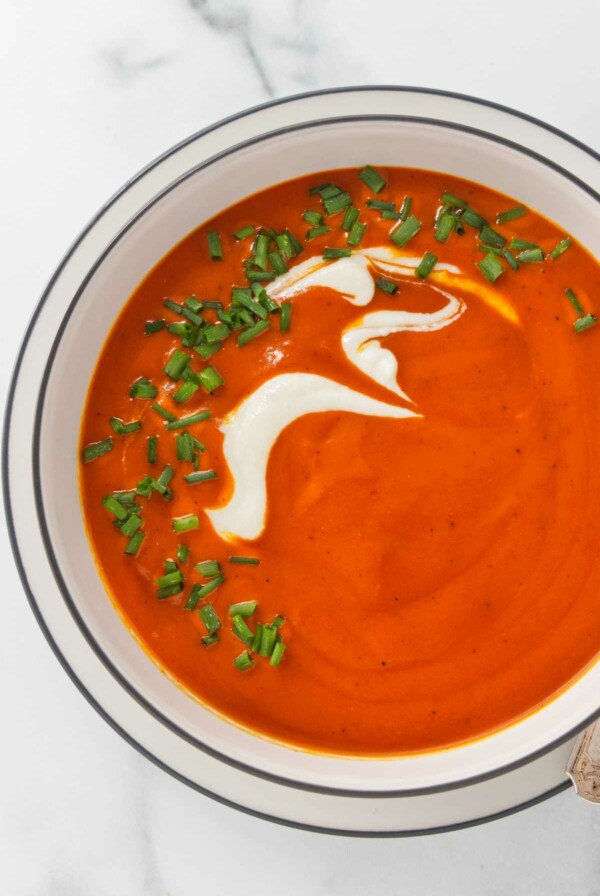 Roasted red pepper soup in a white bowl and garnished with cream and chives.