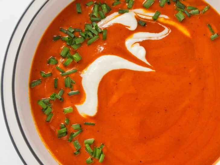 Roasted red pepper soup in a white bowl and garnished with cream and chives.