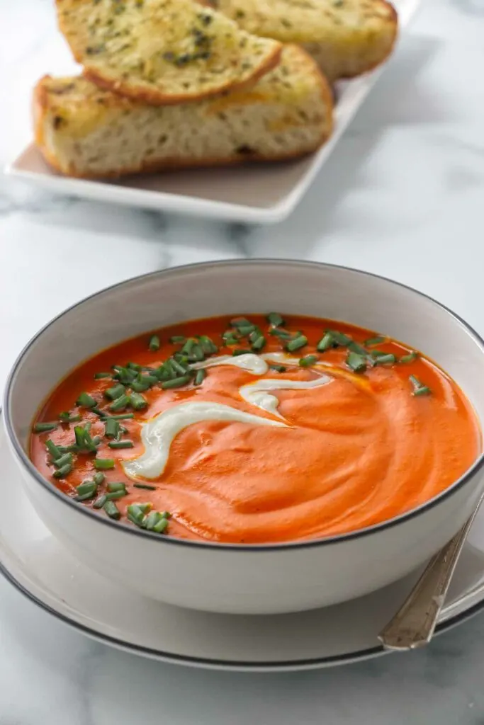 A bowl of red pepper soup with a swirl of goat cheese cream on top.