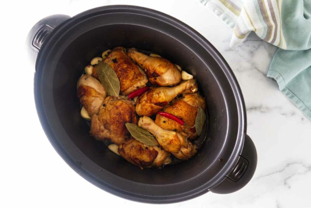 Chicken thighs and chicken legs in a slow cooker with a red chili, peppercorns and bay leaves, ready to cook.