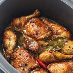 Chicken thighs and chicken legs in a slow cooker with a red chili, peppercorns and bay leaves.