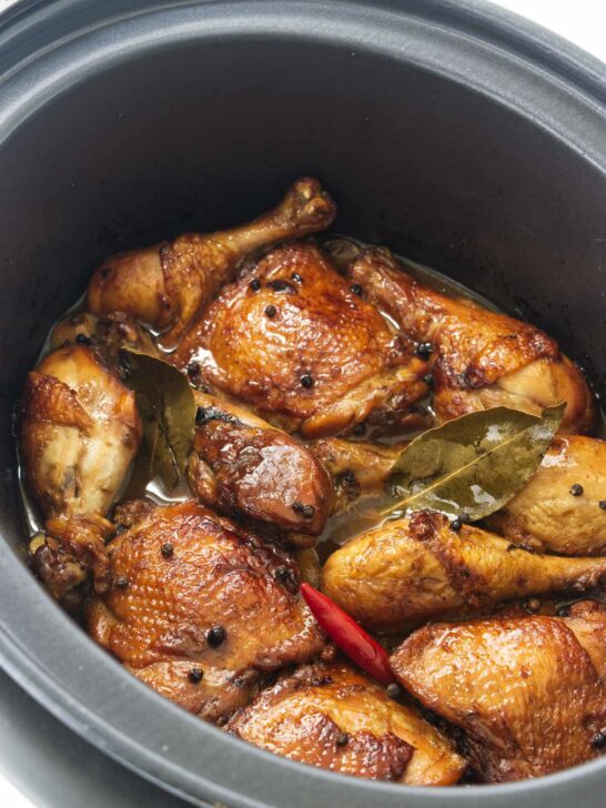 Chicken thighs and chicken legs in a slow cooker with a red chili, peppercorns and bay leaves.