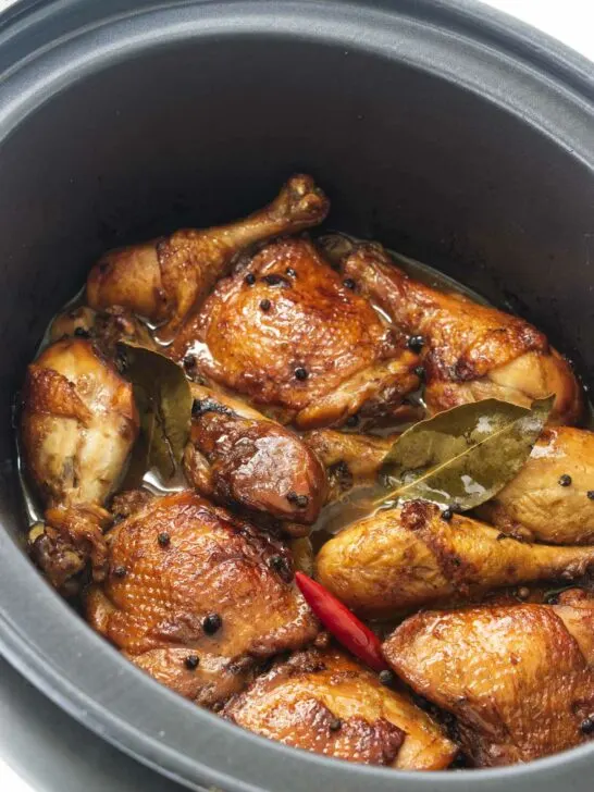 Chicken thighs and chicken legs in a slow cooker with a red chili, peppercorns and bay leaves.