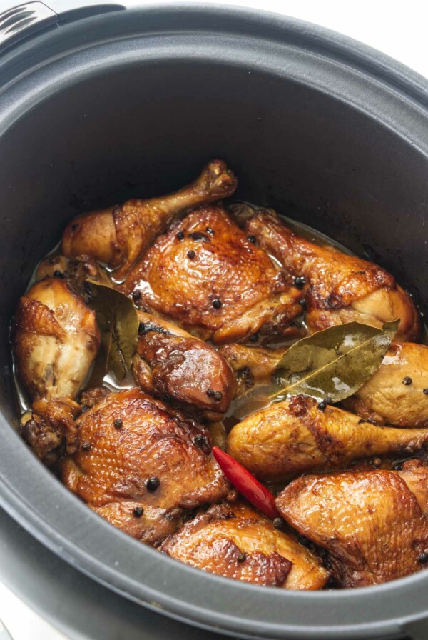 Chicken thighs and chicken legs in a slow cooker with a red chili, peppercorns and bay leaves.