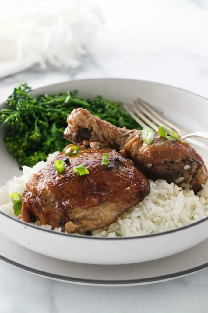 A serving of a chicken thigh and chicken leg on a mound of white rice and broccolini.