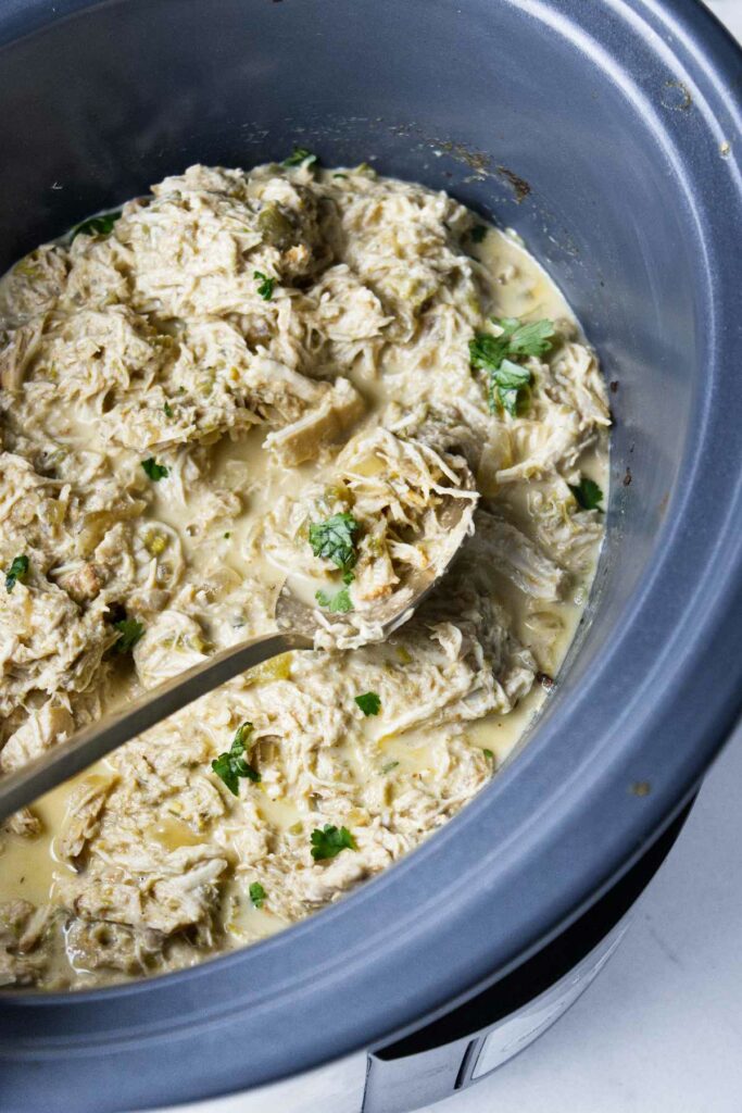 Shredded green chicken chile in a slow cooker with a spoon.