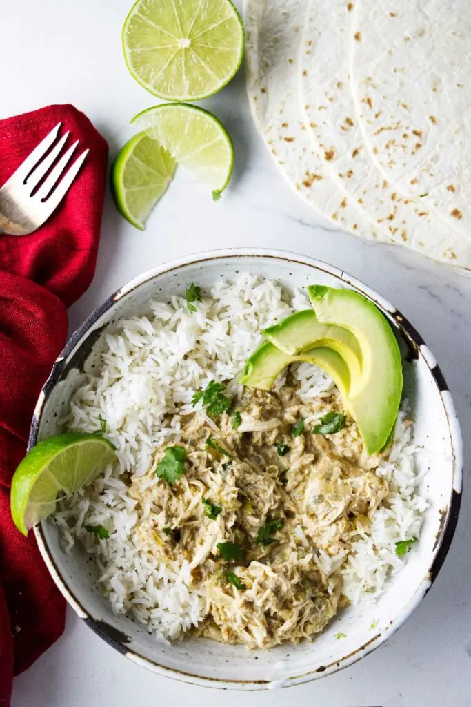 Green chile chicken in a bowl with rice. Tortilla shells and lime slices next to the bowl.