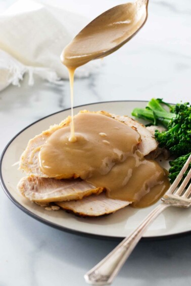 Drizzling gravy over slices of turkey on a plate.